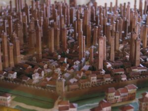 Photo of a model of Bologna, with so many earthy pink tall skinny towers sticking up from every block of the terra-cotta-roofed town that it looks like plant seeds starting to come up in spring. Around the edge you can see the city's moat and battlemented walls, looking tiny compared to the towers which rise to six or seven times the height of the three-story buildings around them.