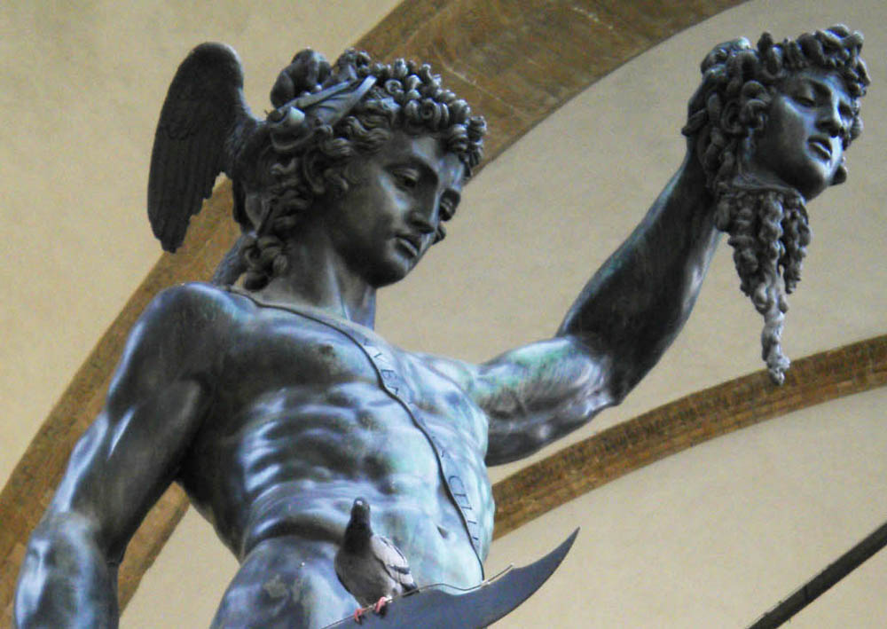 A detailed image of Perseus's torso as he holds up the severed head. You can see the name of the sculptor "Benvenuto Cellini" written on a strap which goes diagonally across Perseus's naked chest, holding his scabbard - the helmet and scabbard are the only clothes he wears. A pigeon sitting on the sword is humorously positioned just in the right spot to hide the penis.