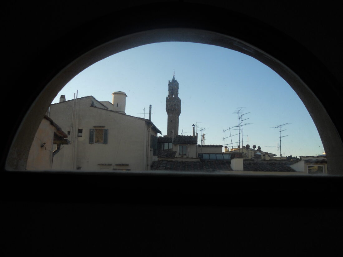 Photograph through a semicircular window, showing a roofline and the tower of Florence's famous Palazzo Vecchio sticking up above. This window was in the bathroom! I had this view from the toilet! It was incredible!