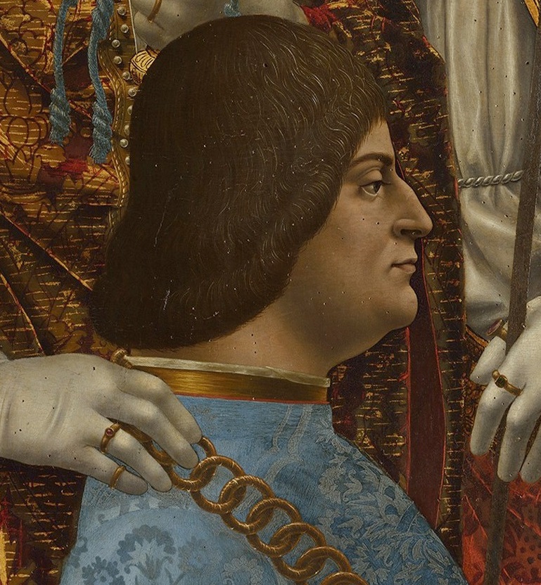 Detail portrait of Ludovico Sforza from the "Pala Sforzesca." Ludovico has black hair down to the nape of his neck, a slightly chubby build, and wears a garment of costly pomegranate pattern light blue silk brocade with gold edging and a huge gold chain around his neck. The background shows the lavish garments of the saints who surround the duke in the complete painting, which shows him and his wife amid religious figures kneeling in prayer.