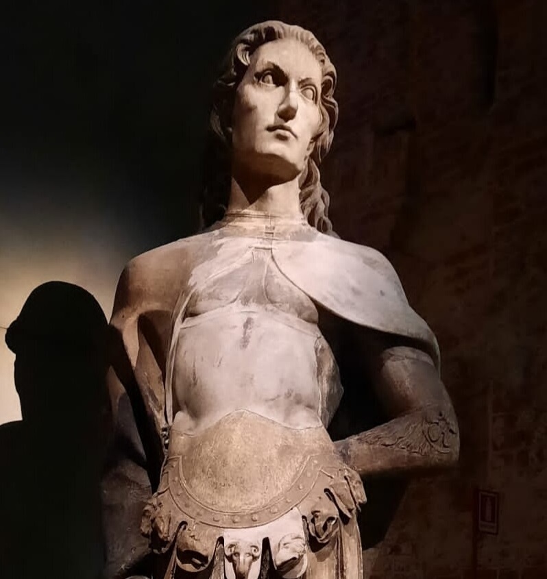 Photograph of a stone statue, probably depicting Galeazzo Sanseverino as the model for Saint Victor the Martyr (statue in Milan cathedral museum). Extremely handsome with shoulder-length curly hair, he wears a cloak over decorated Roman armor, and has his arms bound behind him in a sexy pose, giving him a homoerotic look similar to depictions of Saint Sebastian but more military.