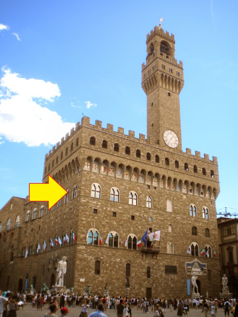 A photograph of Florence's beautiful Palazzo Vecchio, the tall, battlemented stone palace with gorgeous arched windows and a tall tower thrusting boldly up against the clouds. An arrow points out where the room to meet with the priori was located, on an upper floor above the skyline of the rest of the city, meaning a floor above being up 111 steps!