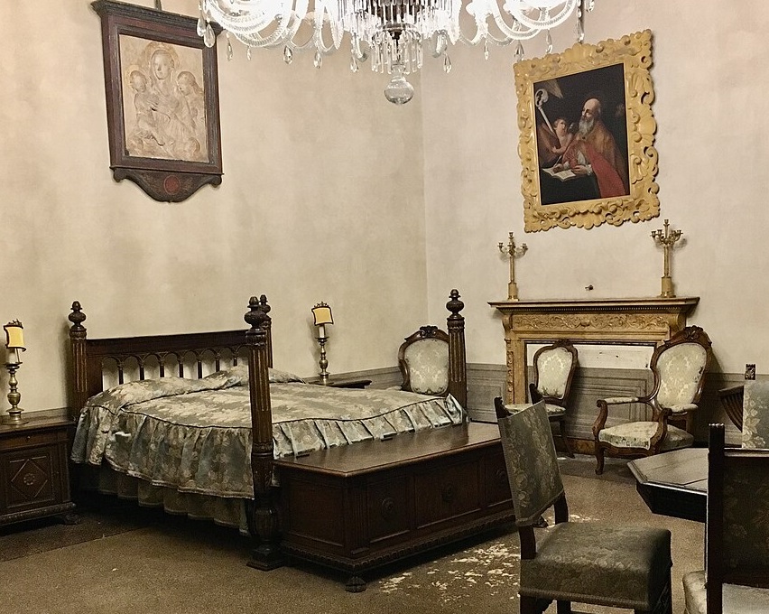 Photograph in the same room in Palazzo Medici, focusing on the large four-poster bed, wider than it is long, built of dark wood with a large chest at the foot of the bed for storage. Around it chairs are gathered, where secretaries could take dictation or visitors meet with the leaders who often used such a bed as their main office. Above the bed hangs a relief carving of the Virgin and Child with angels, and on the wall to the right a painting of Saint Jerome hard at work at his desk as an old man, with an angel helping him. Saint Jerome was a patron saint of scholars, translators, Latin-lovers, and was famous for turning his back on comforts and embracing pain and mortification of the flesh as a way of urging himself to focus on his work and service to the Lord and humanity. The angel helper makes me think of Angelo Poliziano, the famous Homeric poet and dear friend of Lorenzo who often took dictation for him in this room when Lorenzo couldn't lift a pen.