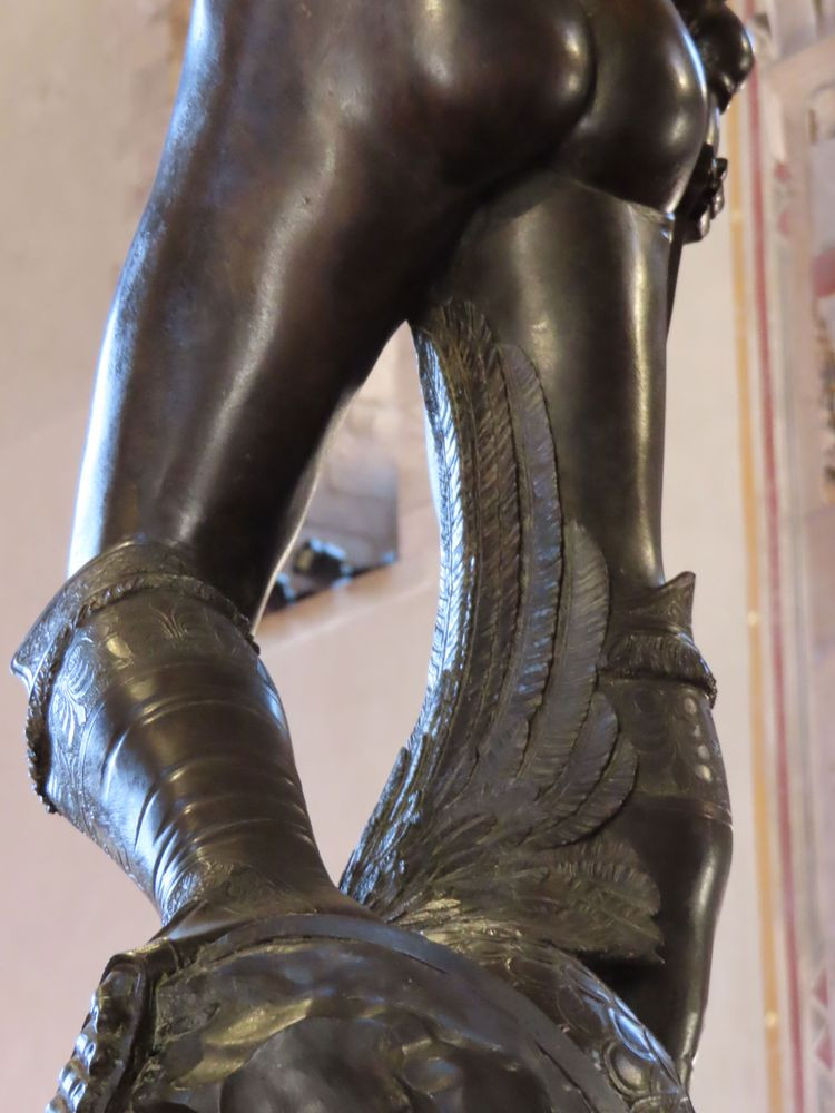 Zoomed in detail of the thighs of Donatello's David, viewed from 3/4 behind. The severed head of Goliath lies at David's feet, and from this angle you can see that the feathers on his winged helmet curve and caress all the way up David's inner thigh stopping about an inch from his crotch, making it impossible not to think about the ticklish sense of touch of feathers on extremely-sensitive skin.